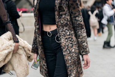 A woman wearing a black crop top and black pants with a leopard-printed coat.