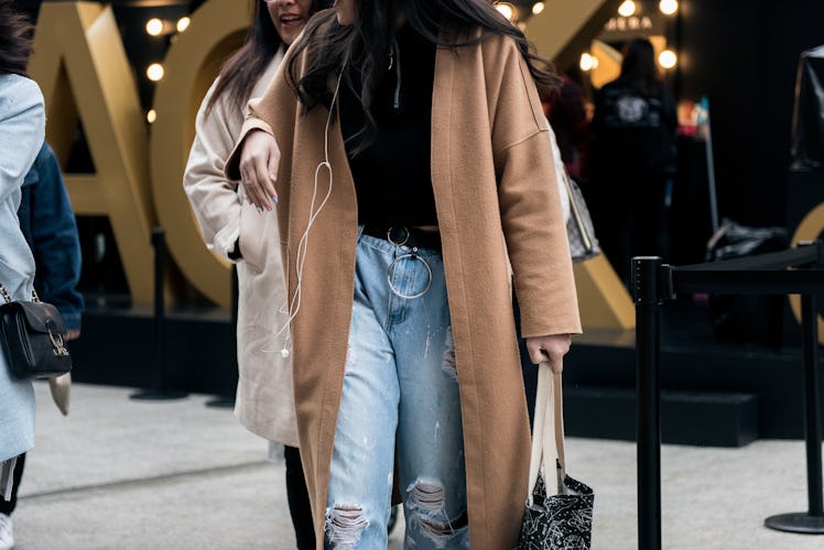 A woman in denim jeans, black t-shirt and a camel coat walking the street in Seoul.