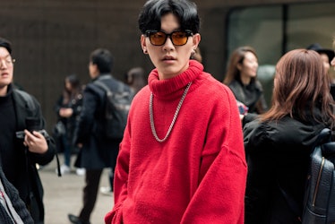 A man wearing an oversized red turtleneck with a silver necklace posing for a photo.