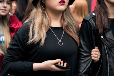 A woman wearing a black hat and a black t-shirt with a silver chain necklace walking the street in S...