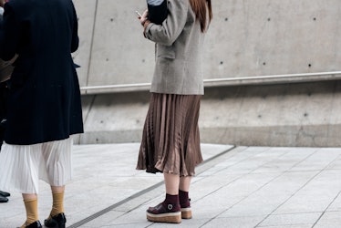Two women wearing matching pleated skirts in beige and white on the street of Seoul.