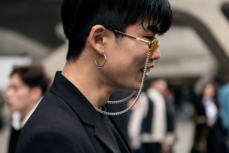 A man with a piercing in his ear, wearing sunglasses with a chain and a black suit