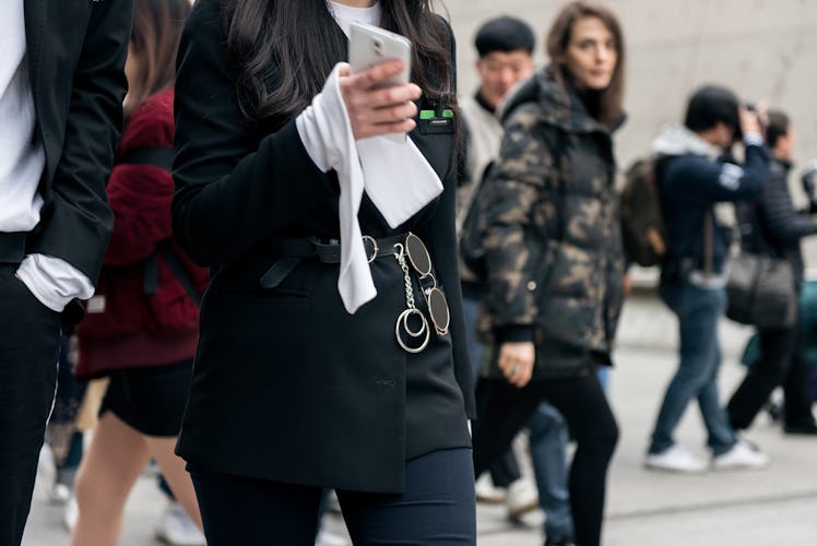A woman wearing a belt with a chain walking the street while looking at her phone