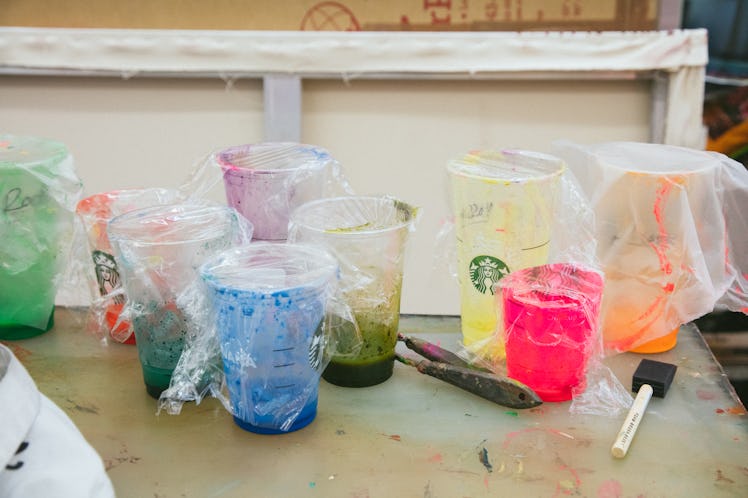 Various plastic cups filled with paint and covered with more plastic on a brown table