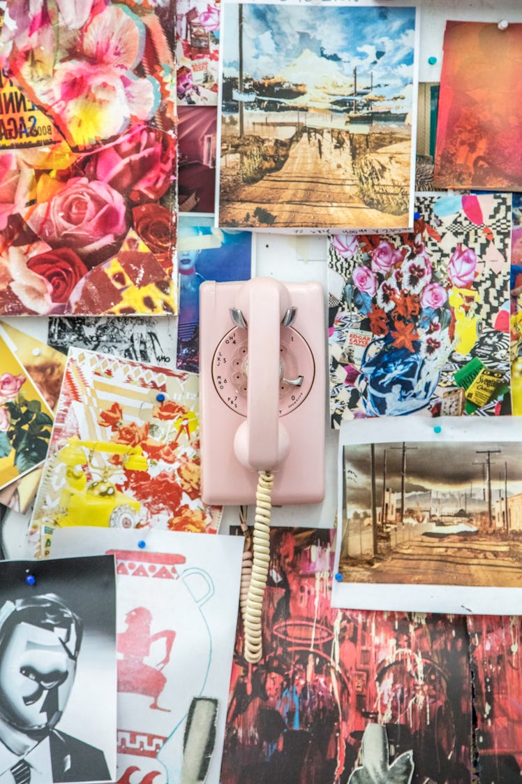 A wall decorated with several photographs and sticker and a pink telephone