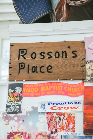 The inside of Rosson Crow studio with a 'Rosson's Place' wooden table and various stickers on a wall