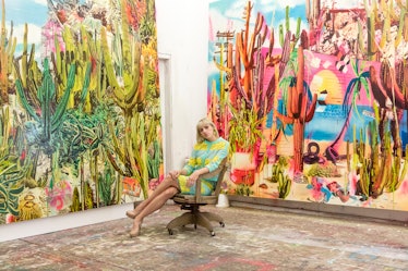 A woman in a blue-yellow floral shirt sitting in a chair with two paintings around her in the Rosson...