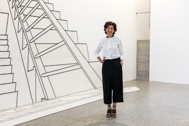 Fernanda Feitosa in a white button-up and black pants posing next to a wall with a ladder drawn on i...