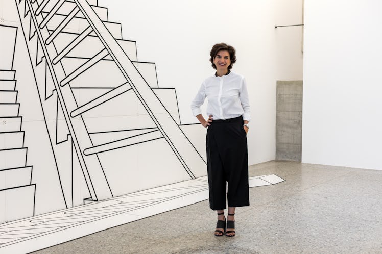 Fernanda Feitosa in a white button-up and black pants posing next to a wall with a ladder drawn on i...