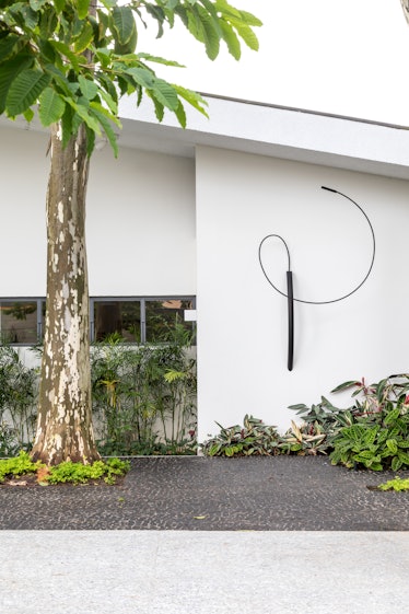 One of the walls of Fernanda Feitosa's house with a black wire sculpture on it that resembles a whip...