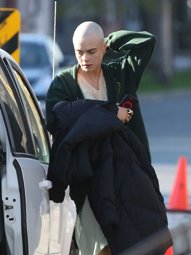Cara Delevingne bald in a green jacket entering a vehicle