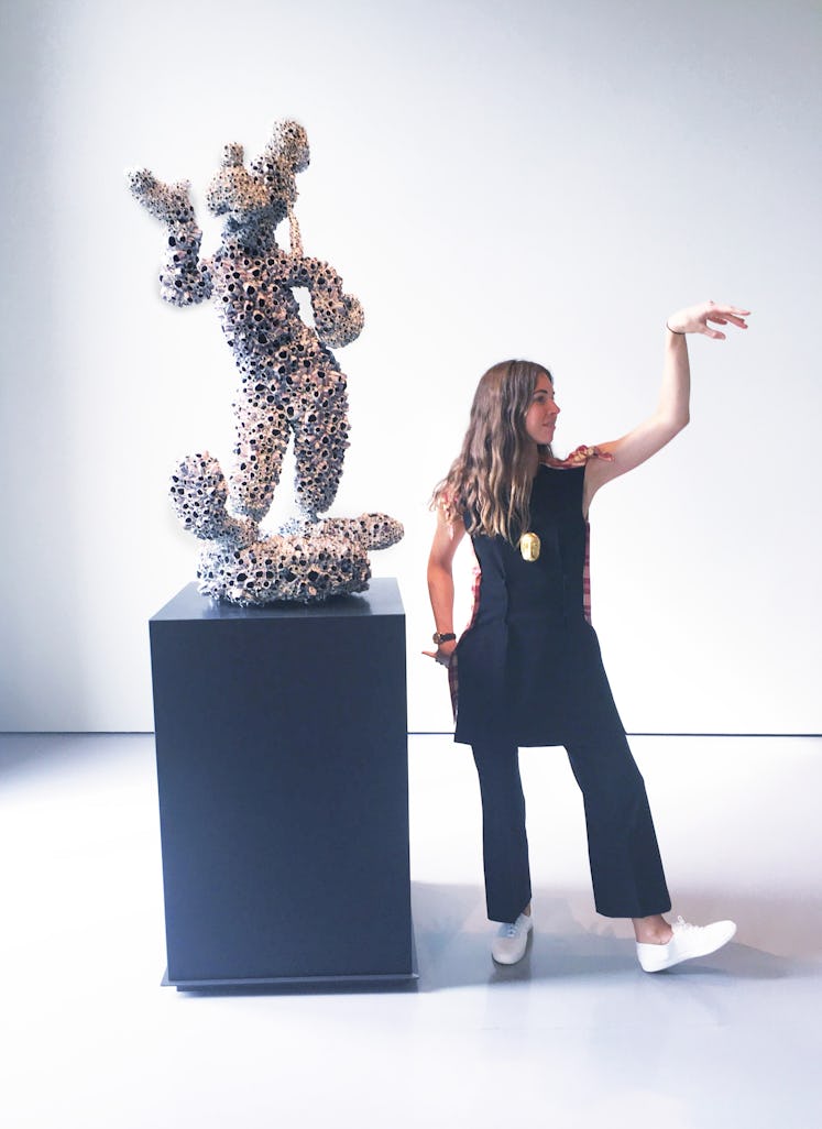 Colby Mugrabi posing next to a coralized sculpture of Goofy by Damien Hirst