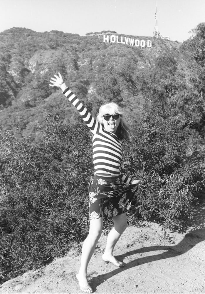 Debbie Harry posing in a white-black striped shirt and a floral skirt with the Hollywood sign in the...