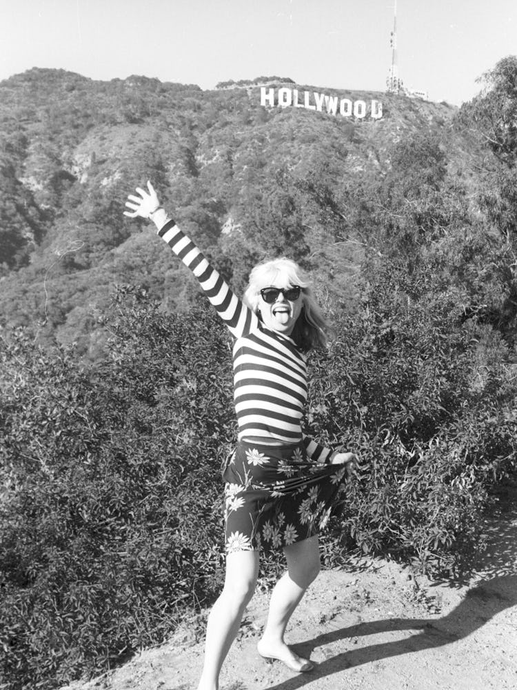 Debbie Harry posing in a white-black striped shirt and a floral skirt with the Hollywood sign in the...
