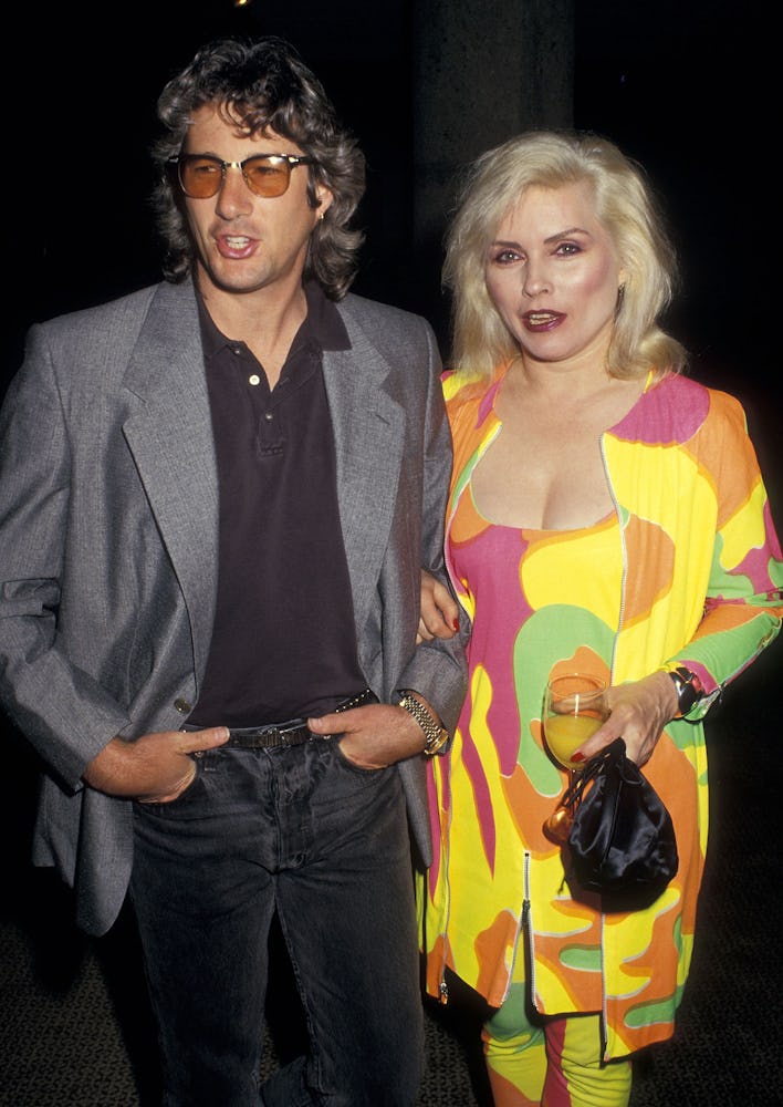 Debbie Harry in a yellow-pink-green multi-color dress and Richard Gere in a black shirt and pants an...