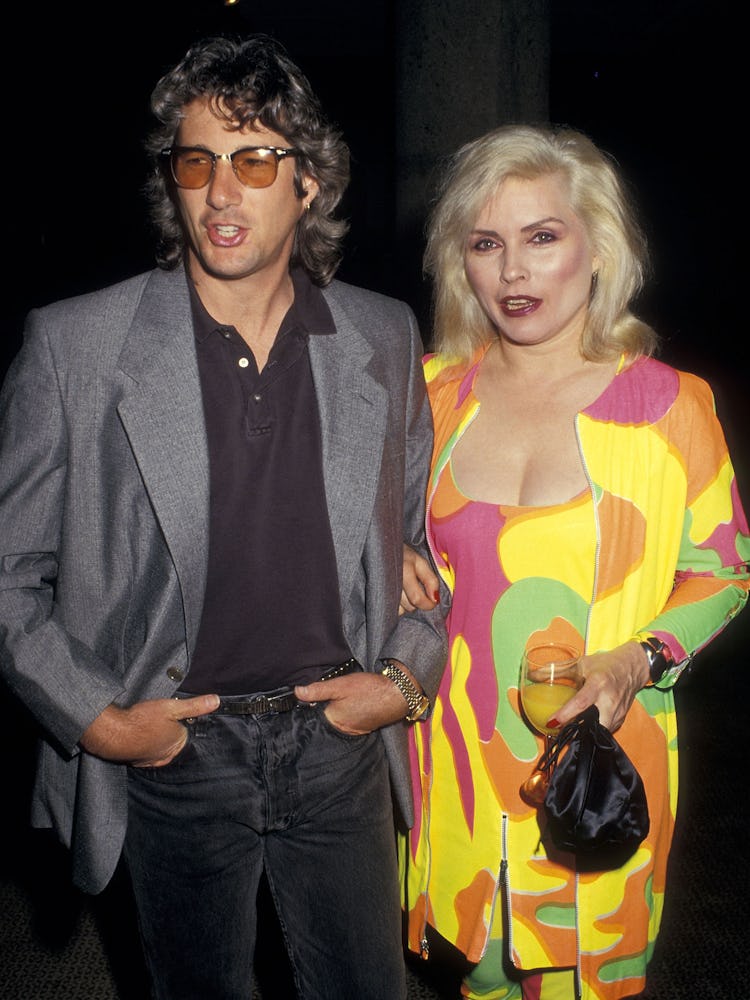 Debbie Harry in a yellow-pink-green multi-color dress and Richard Gere in a black shirt and pants an...