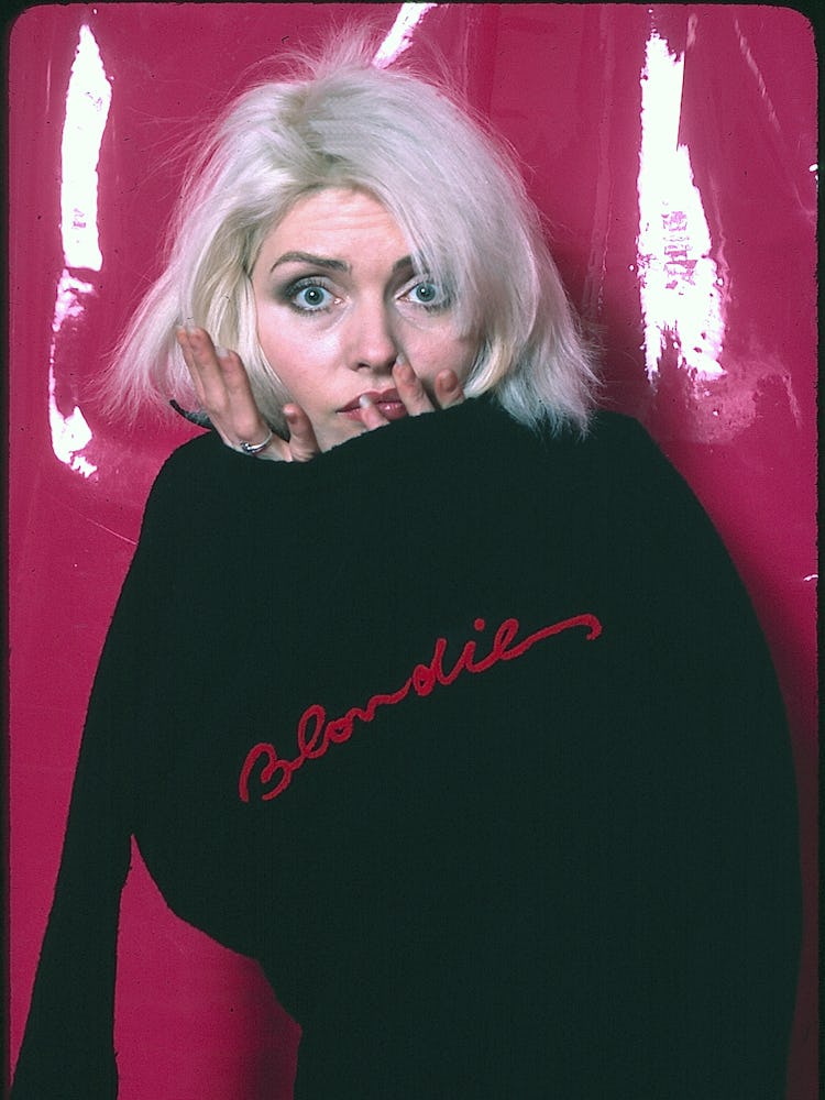 Debbie Harry posing in a black sweater with the word 'Blondie' embroidered in red