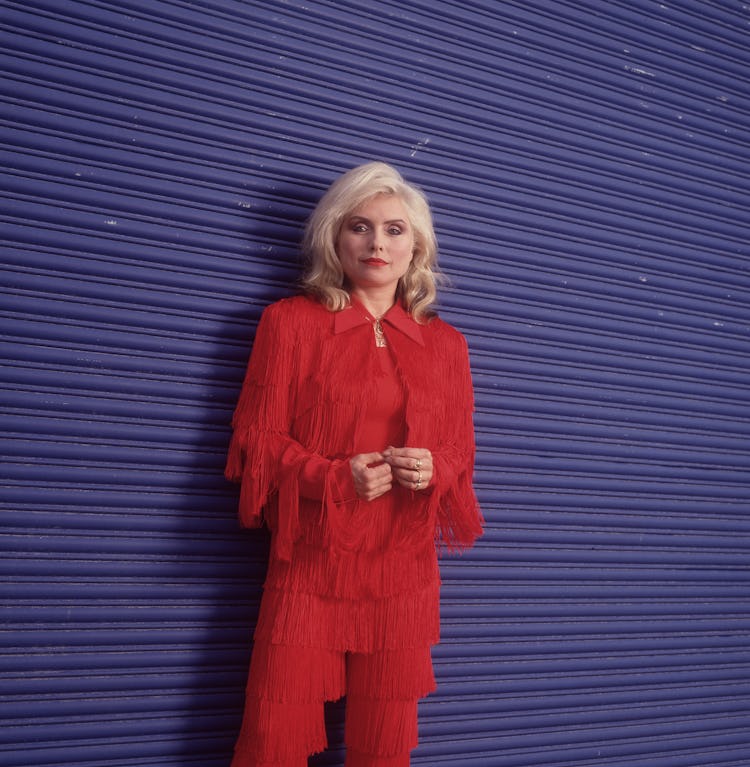Debbie Harry in a red fringed suit standing in front of a blue striped wall