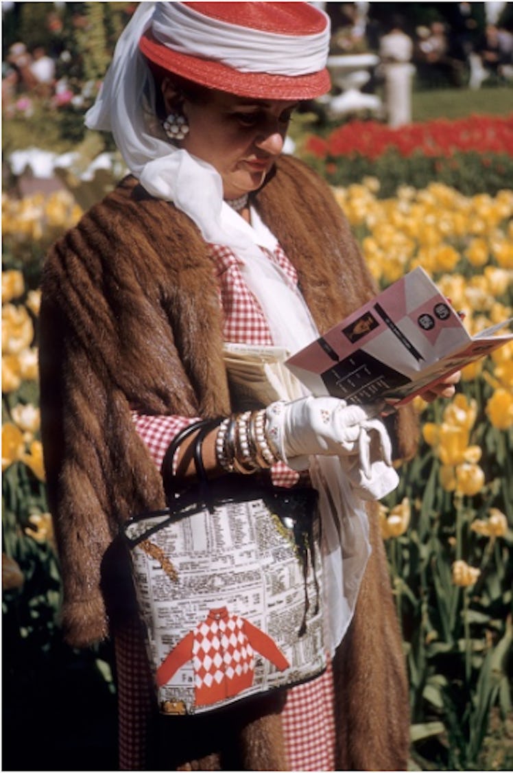 A woman in a brown fur coat, red-white had and back, looking at a notebook at the Kentucky Derby in ...