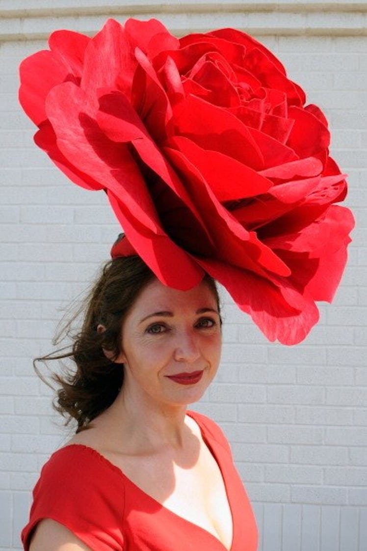 A brunette woman in a red dress and oversized red flower hat the Kentucky Derby in 2014.