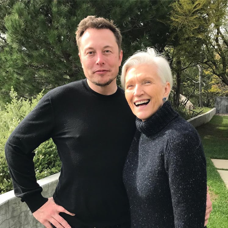 Maye Musk in a black sweater posing and smiling next to Elon Musk in a black shirt