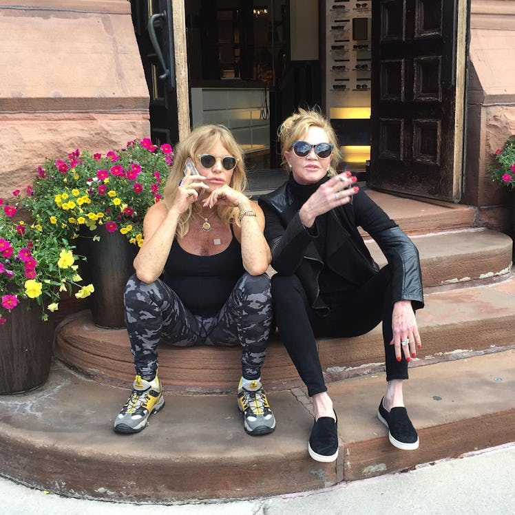 Goldie Hawn and Melanie Griffith sitting on steps of a restaurant entrance during the day and posing...
