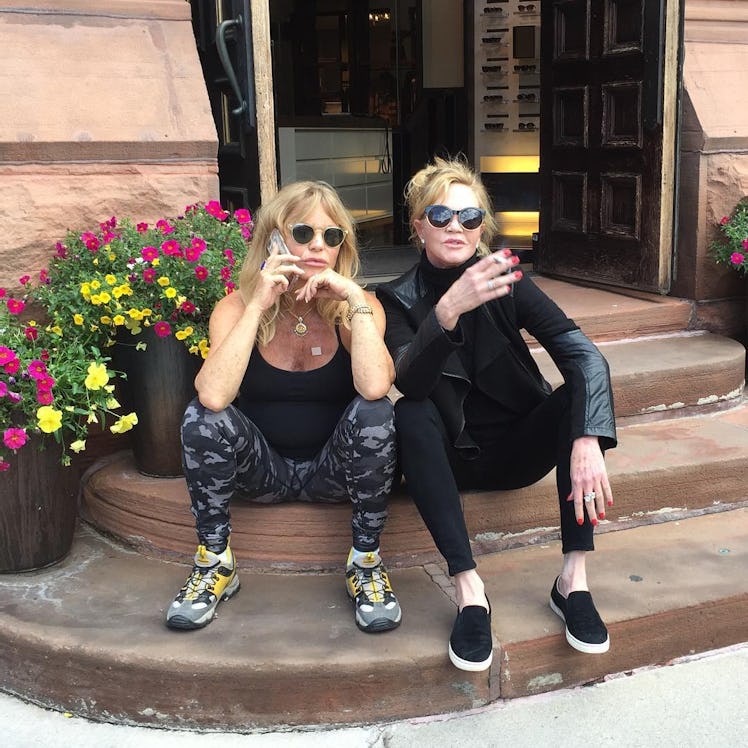 Goldie Hawn and Melanie Griffith sitting on steps of a restaurant entrance during the day and posing...