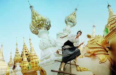 Edie Campbell posing on wooden stairs in a long skirt and white shirt while surrounded by gold detai...