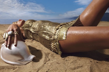 Model lying down on a sand beach in golden dress while holding a seashell 