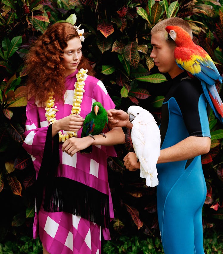 Natalie Westling holding a green parrot in Hawaii, with a blonde haired boy next to her holding two ...