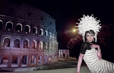 Edie Campbell posing in Rome in front of Colosseum with a huge white headpiece decoration