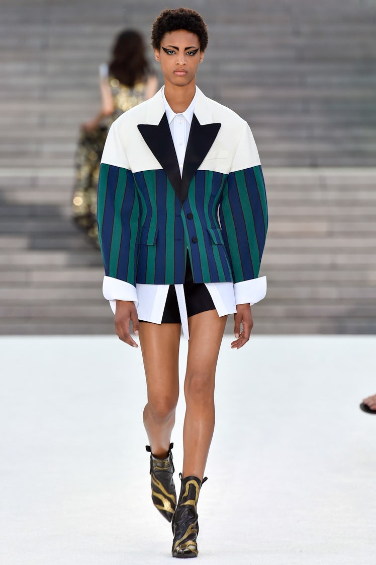 A female model walking a runway while wearing a striped jacket in white, navy, and forest green with...