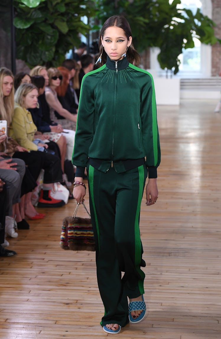 A female model walking a runway while wearing a green Valentino sporty tracksuit