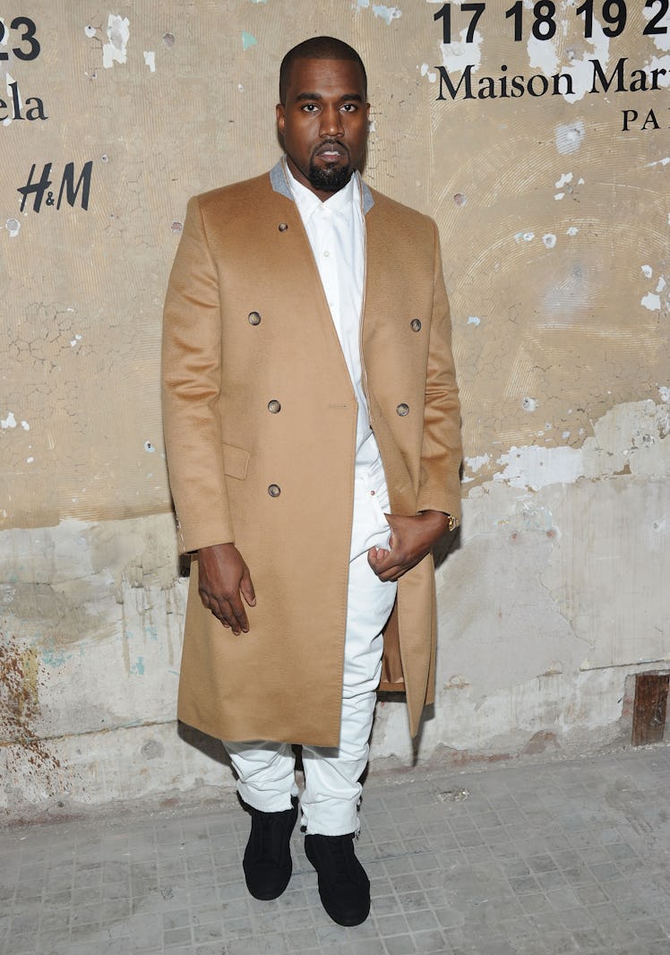 Kanye West in a white shirt and trousers and a camel coat in 2012