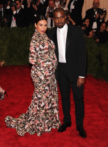 Kanye West in a black suit and a white shirt and Kim Kardashian in a floral red-white-black dress at...