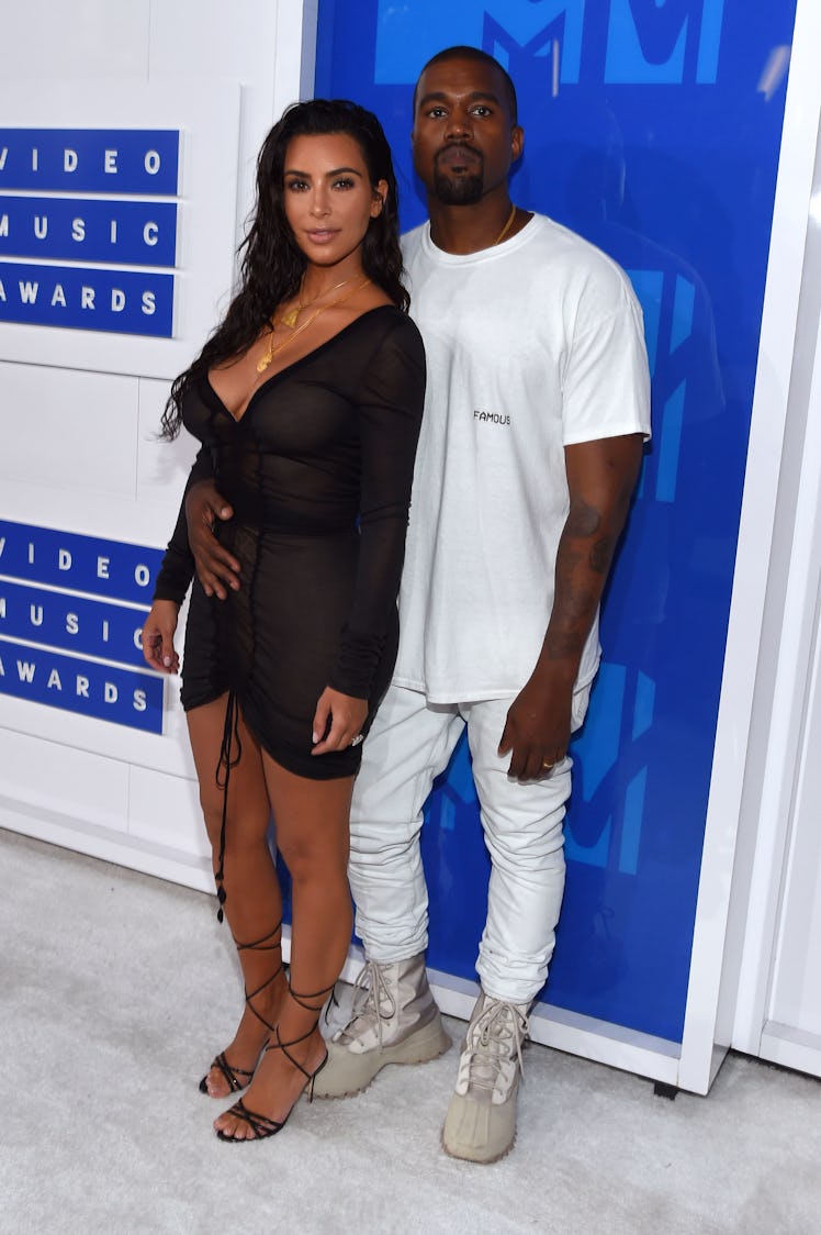Kanye West in a white shirt and pants and beige sneakers and Kim Kardashian in a sheer black dress a...