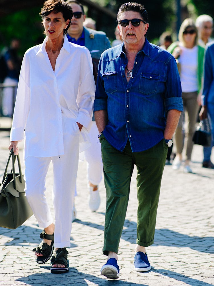 A woman in a white shirt and pants and a man in a denim shirt and green pants walking