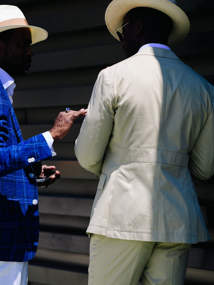 The back of a man wearing a beige suit and a man wearing a blue blazer and white pants