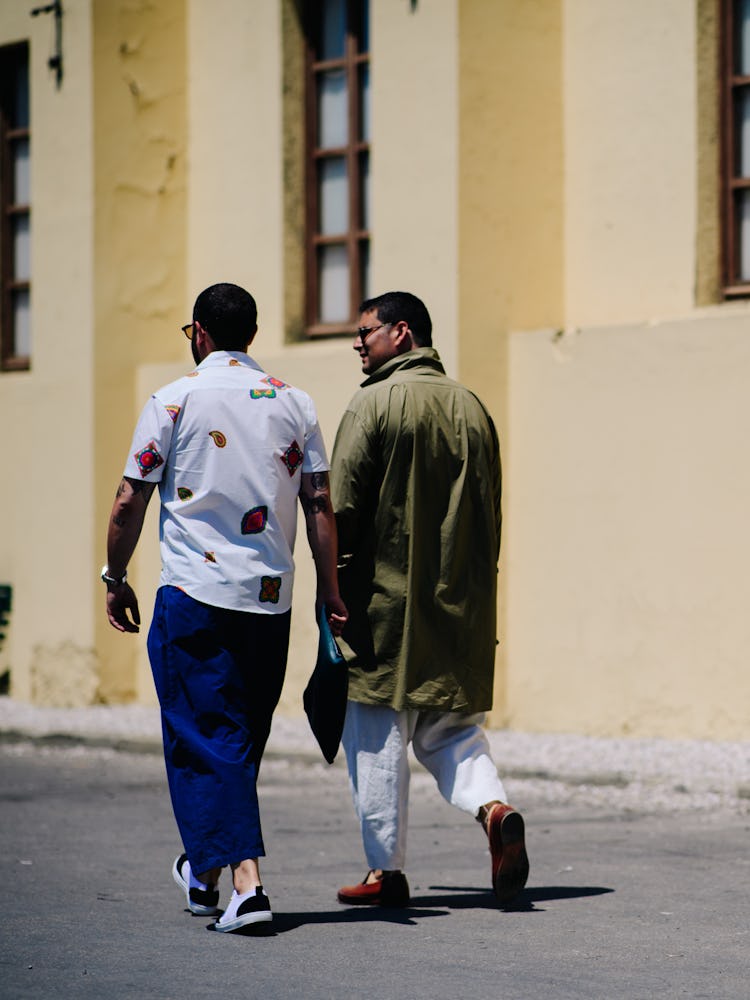 The back of two men walking in the distance wearing a green jacket and a white shirt