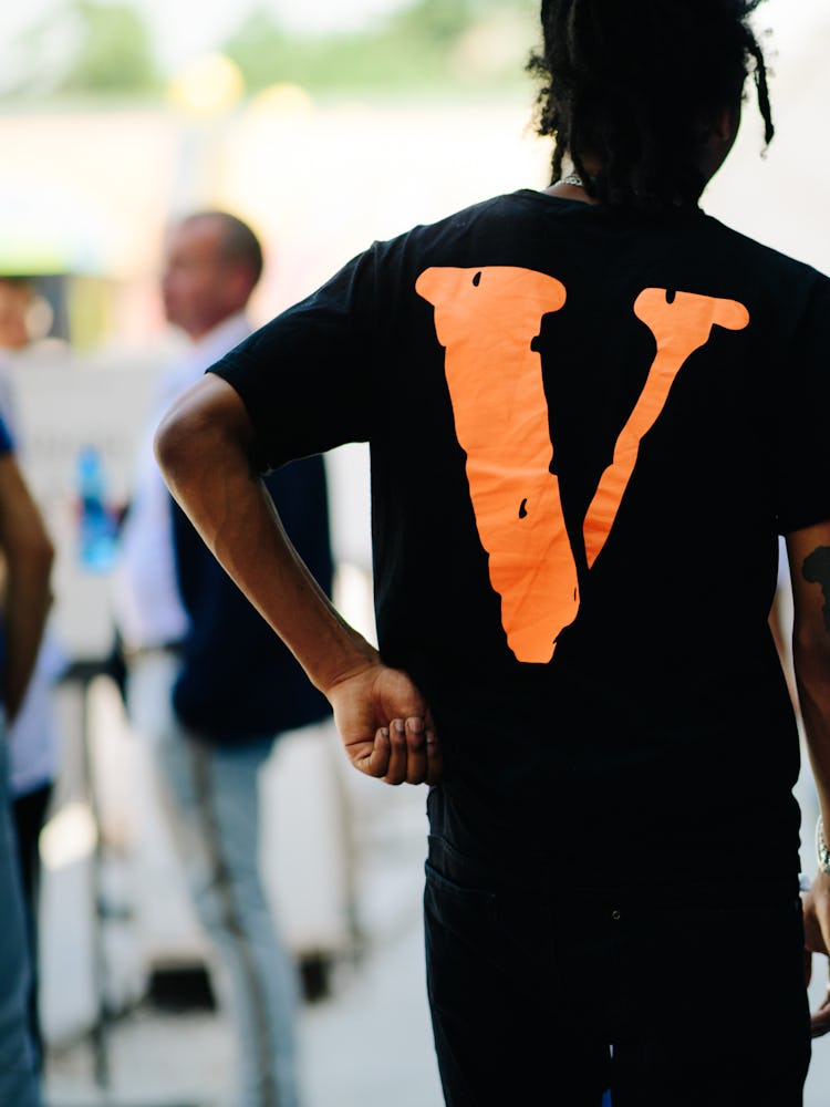 The back of a man in a black shirt with an orange 'V' and a man in a white shirt with a black backpa...