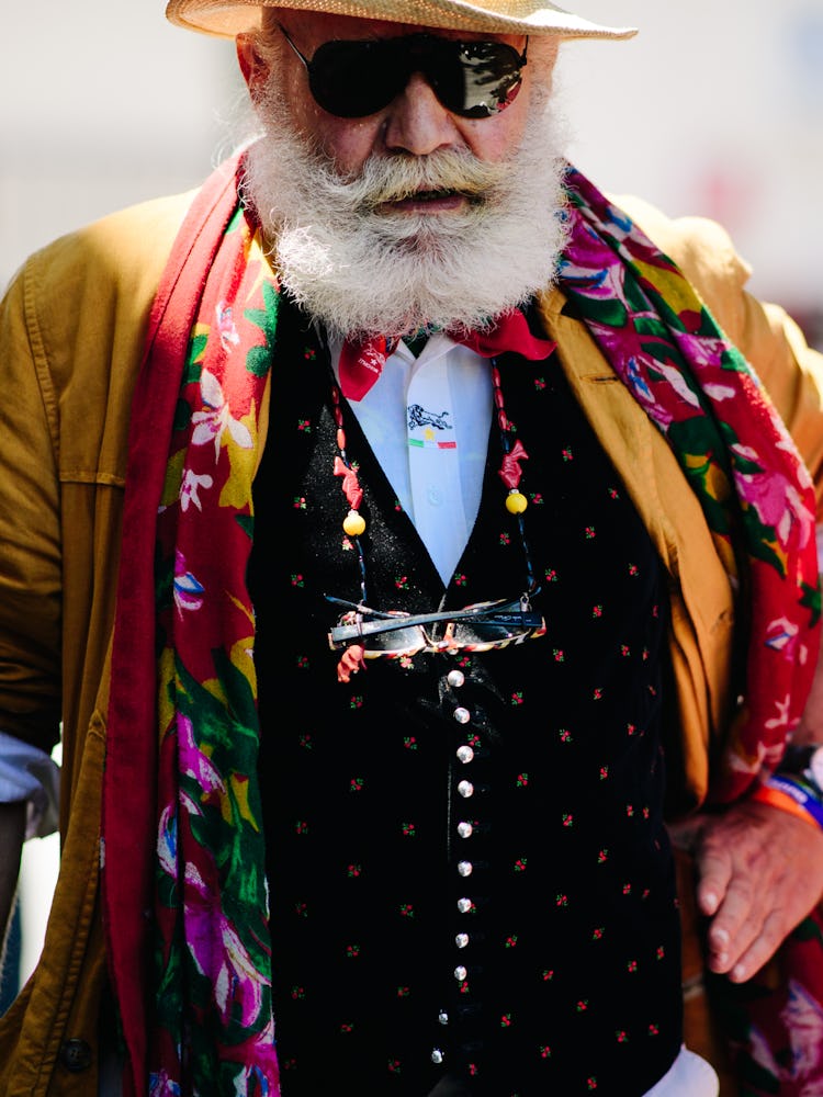 A bearded man in a black waistcoat, an orange blazer and a floral scarf