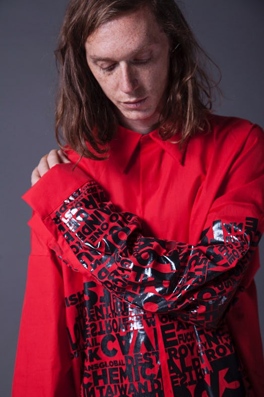A brunette model wearing a red shirt with black letter print by Omar. looking down