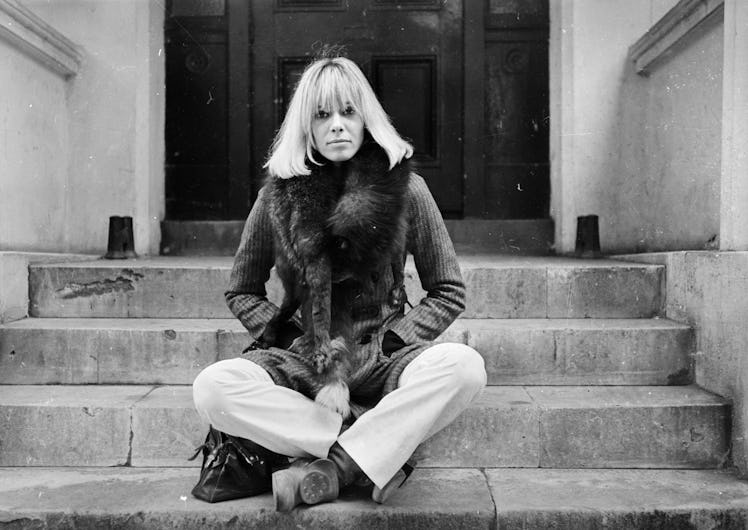 Anita Pallenberg in a jacket and trousers sitting on steps in black and white
