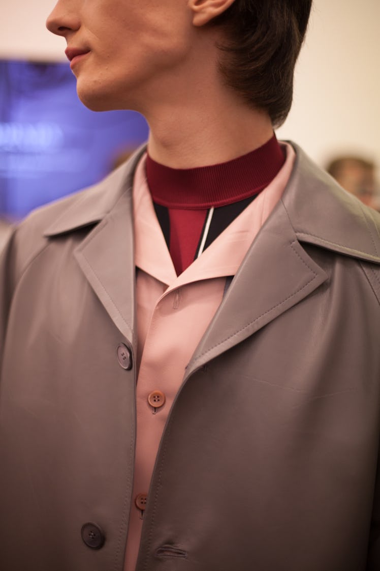 A close-up of a model wearing a grey jacket, pink shirt and black-red top at the Prada Spring/Summer...