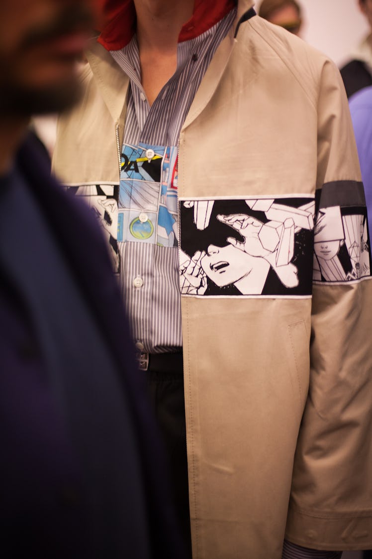 A model wearing a striped blue shirt and a beige jacket with comic print element at the Prada Spring...