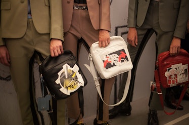 Three models in an olive, pink and grey suit holding bags backstage at the Prada Spring/Summer 2017 ...
