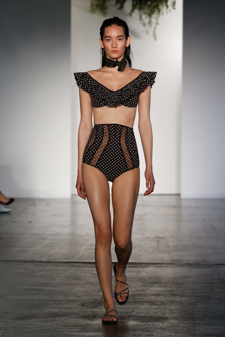 A female model walking a runway in a black top and black underpants