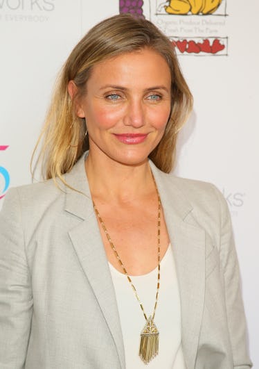 Cameron Diaz at a red carpet, wearing a beige blazer, low-cut white shirt and a long golden necklace...