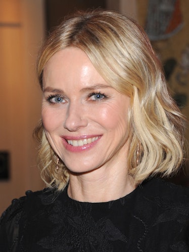 Naomi Watts wearing subtle makeup, golden hoop earrings and a black velvet top with embroidered flow...