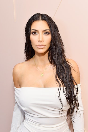 Kim Kardashian West at an event wearing an open-shoulder white dress, a thin gold necklace and sport...